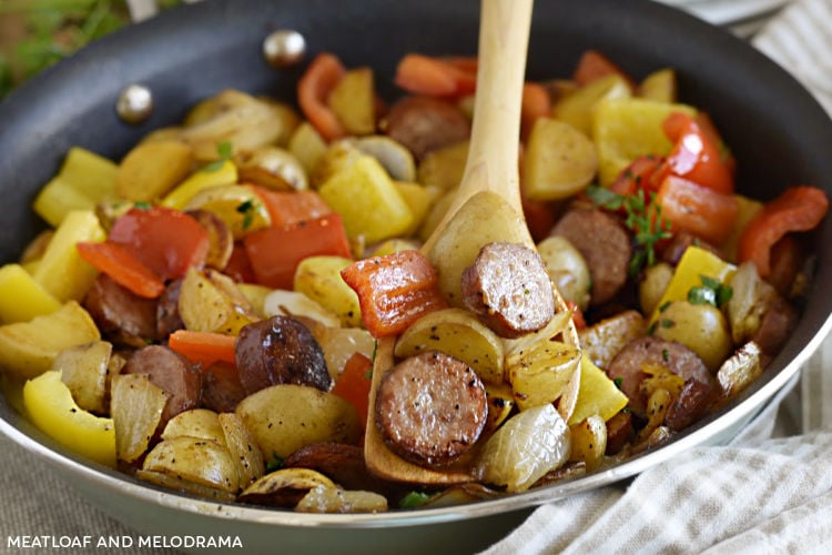 fried kielbasa with potatoes, peppers and onions on wooden spoon in a skillet