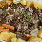 oven baked chuck roast with baby carrots, potatoes, celery and onions on a white platter