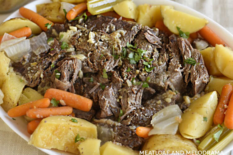 oven baked beef chuck roast with baby carrots, potatoes, celery and onions on a white platter