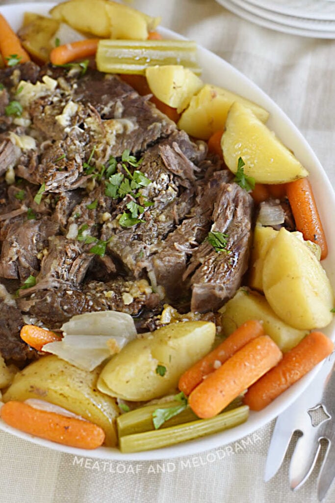 oven baked beef chuck roast on a platter with carrots, potatoes and celery