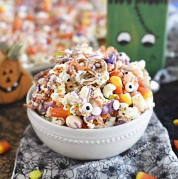 monster munch halloween snack mix made with popcorn, pretzels and candy in a white bowl with halloween decorations