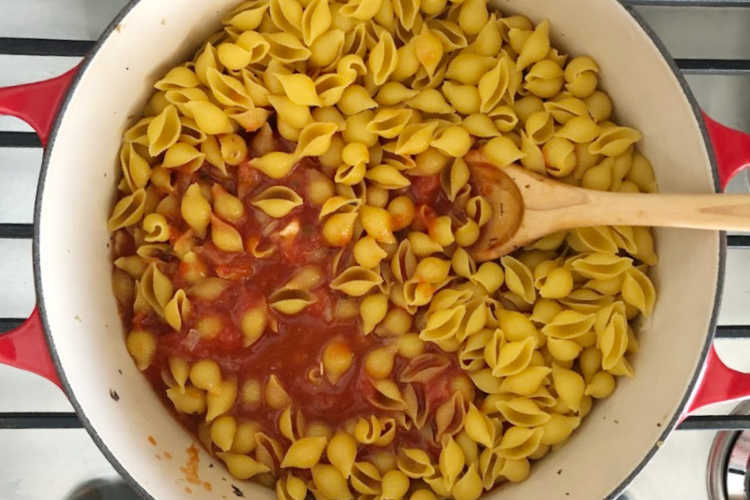 pasta shells and tomato sauce in a red dutch oven with wooden spoon