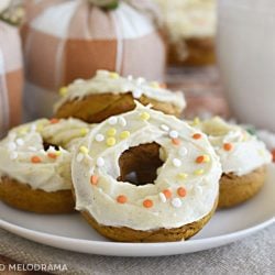 pumpkin spice cake mix donuts with cream cheese frosting and fall sprinkles on a white plate with cloth pumpkins