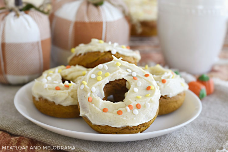pumpkin spice cake mix donuts with cream cheese frosting and fall sprinkles on a white plate with cloth pumpkins