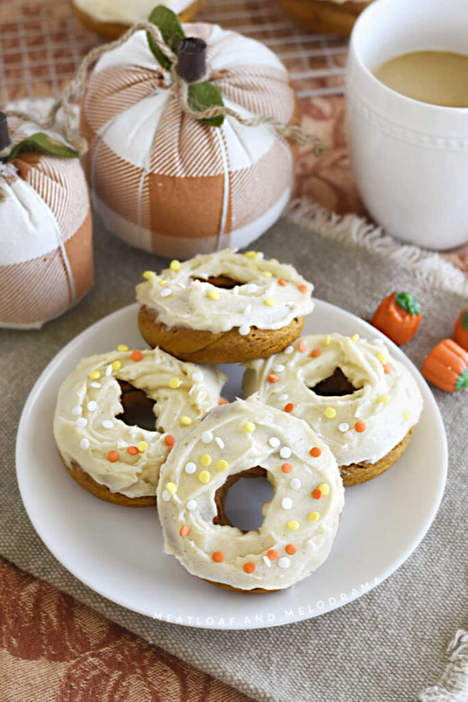 2 ingredient pumpkin donuts with cream cheese frosting on a white plate with cloth pumpkins in the background