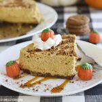 instant pot pumpkin cheesecake with gingerbread crust on a white plate with whipped cream, caramel and marshmallow pumpkins