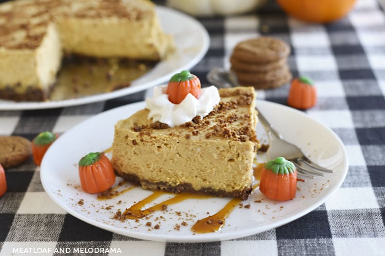 instant pot pumpkin cheesecake with gingerbread crust on a white plate with whipped cream, caramel and marshmallow pumpkins