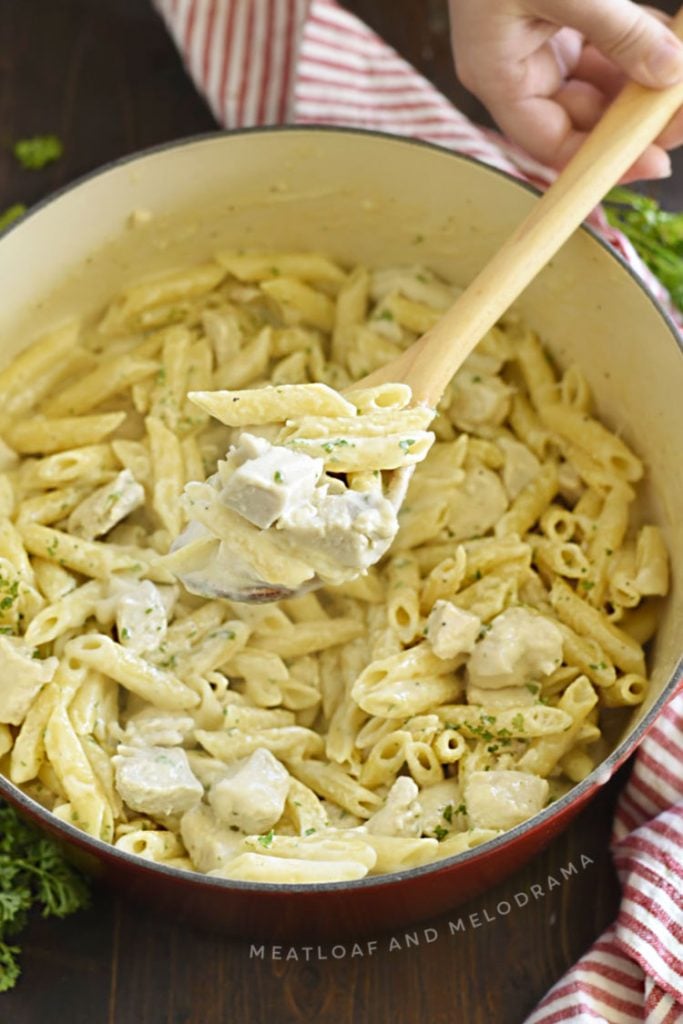 chicken alfredo penne pasta on a wooden spoon in dutch oven