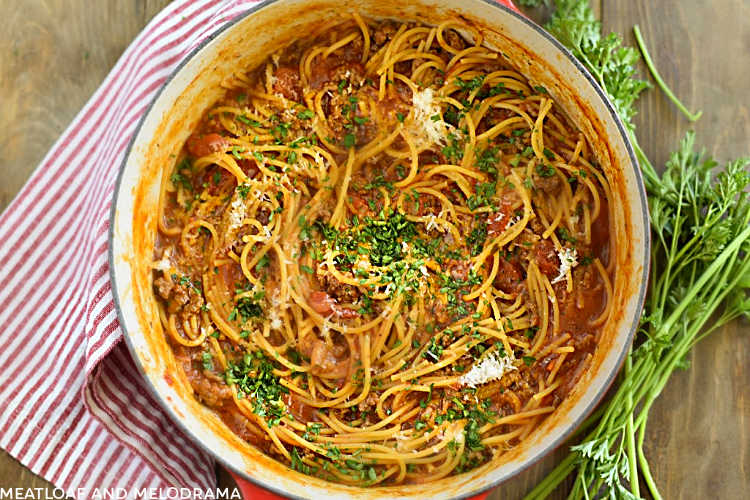 one pot spaghetti and meat sauce topped with Parmesan cheese and parsley in red dutch oven