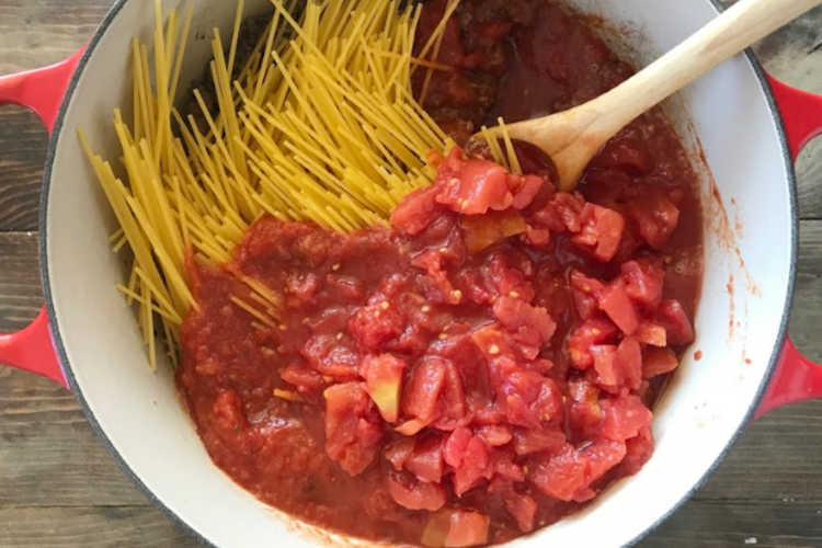 uncooked spaghetti noodles with diced tomatoes, pasta sauce and meat in red dutch oven