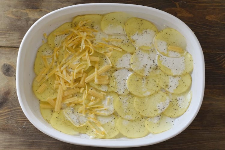 thinly sliced potatoes in a baking dish with cream and shredded cheese