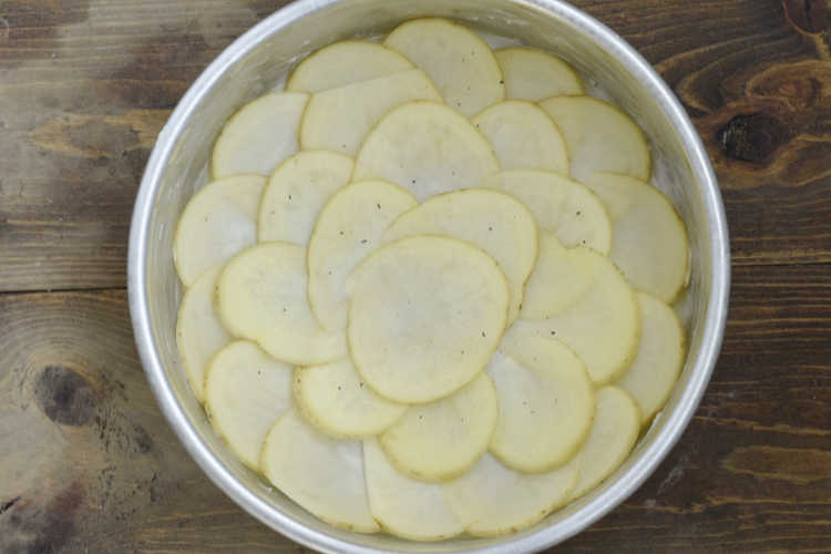 thinly sliced potatoes in round cake pan
