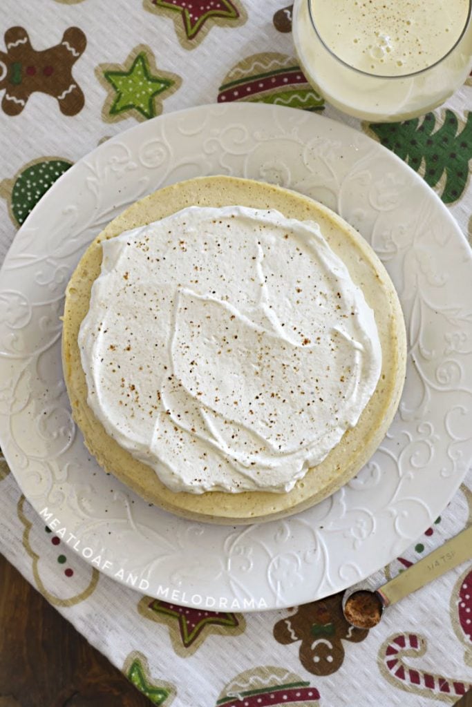 eggnog cheesecake with eggnog whipped cream on a white plate