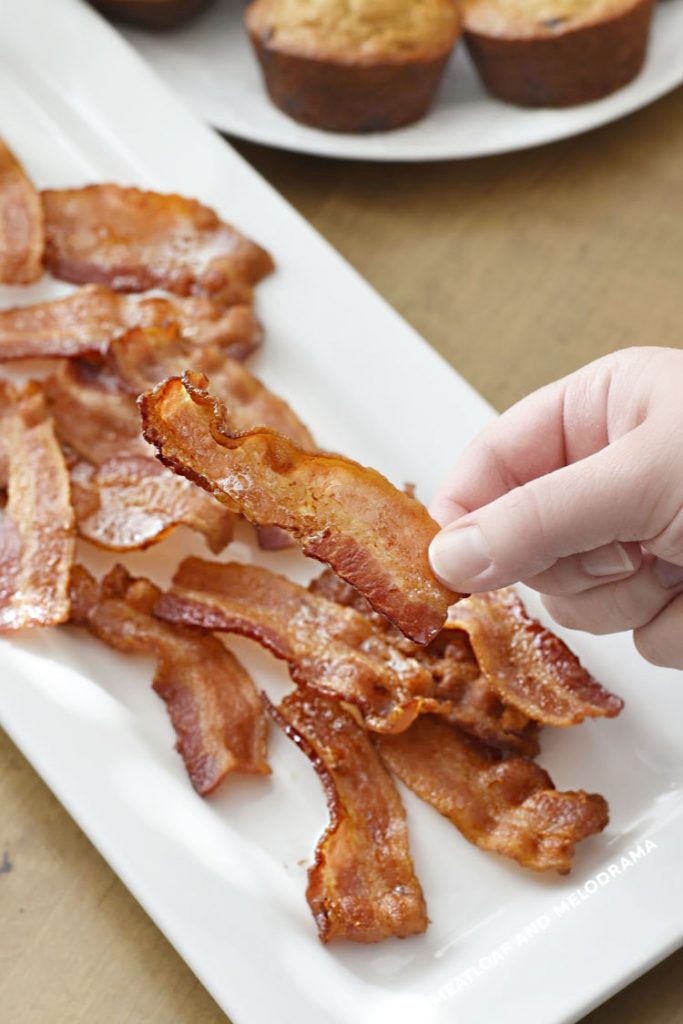 cooked bacon in hand over platter of crispy bacon