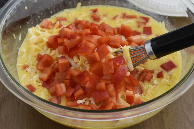 red peppers and shredded cheese with scrambled eggs in a mixing bowl