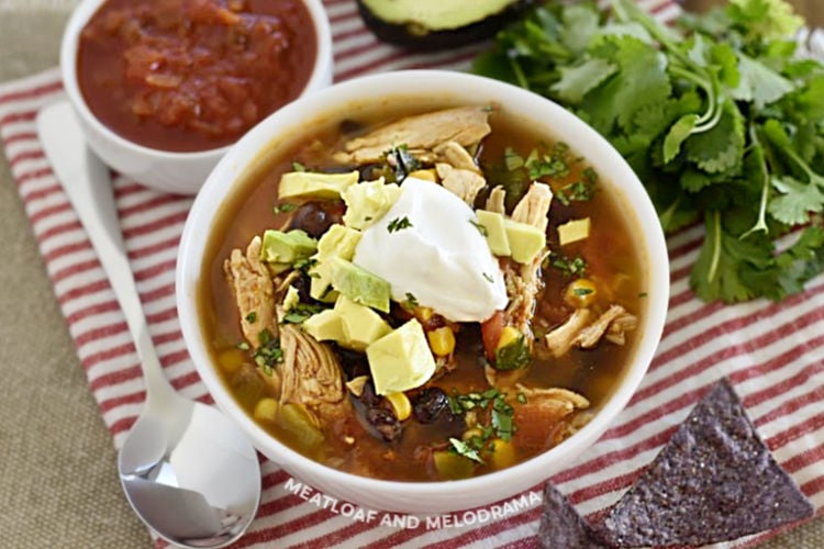 chicken taco soup with black beans and corn topped with sour cream and avocado in a white bowl