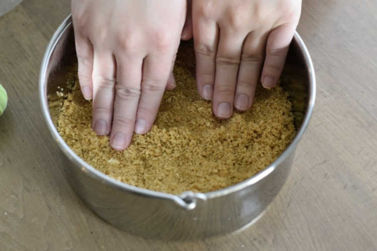 hands pressing graham cracker crust into 7 inch springform pan
