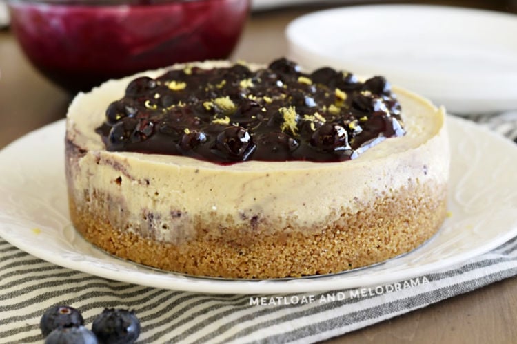 lemon cheesecake topped with homemade blueberry sauce and lemon zest on platter