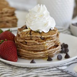 chocolate chip pancakes with whipped cream and strawberries on white plate