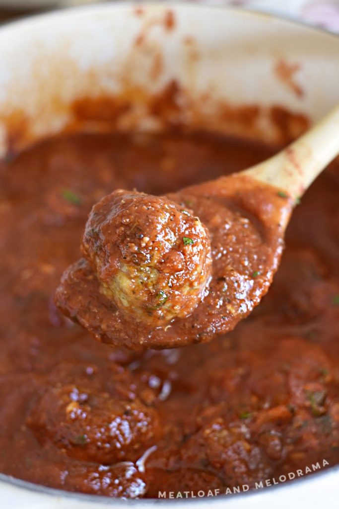 meatball in sauce in wooden spoon over dutch oven