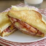 fried bologna sandwich with provolone cheese and tomato on toasted bread on a plate