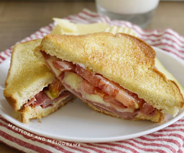 fried bologna sandwich with provolone cheese and tomato on toasted bread on a plate