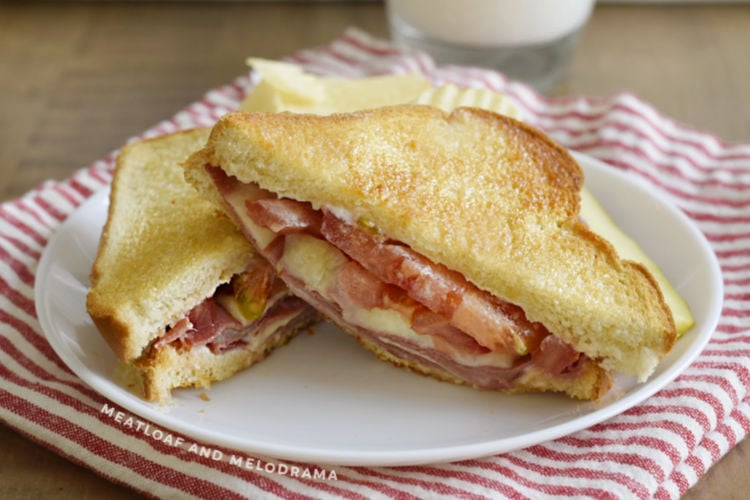 fried bologna sandwich with provolone cheese and tomato on toasted bread on a plate