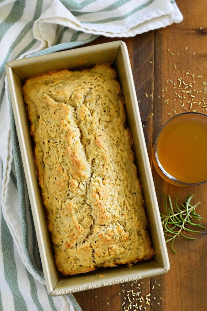 baked rosemary bread in loaf pan with glass of beer on the side