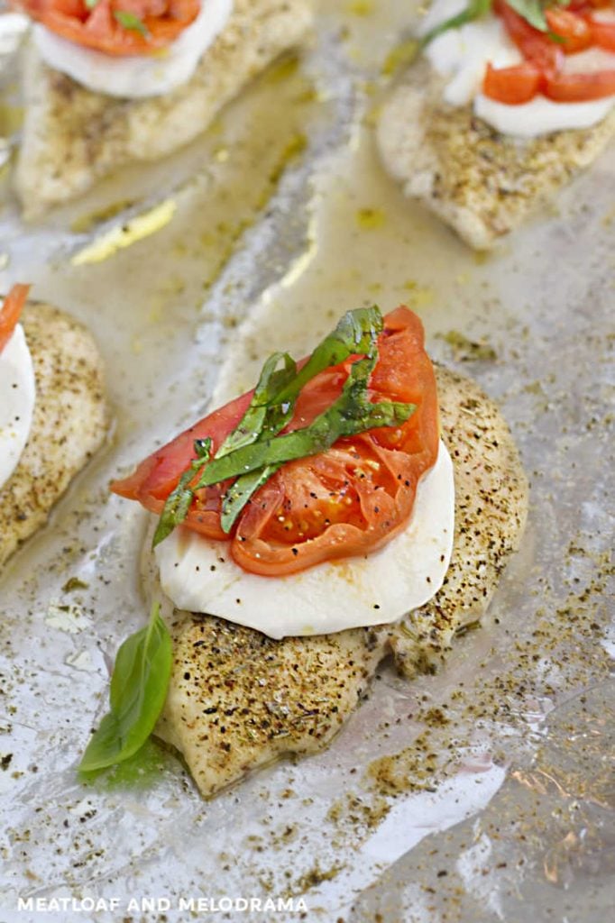 chicken breasts topped with mozzarella, tomatoes and basil on a sheet pan