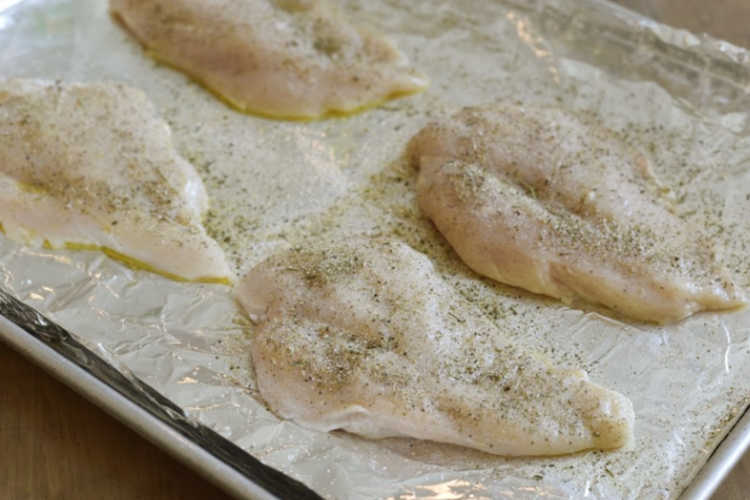 seasoned uncooked chicken breasts on a sheet pan