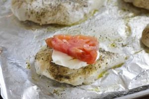 baked chicken breasts with fresh mozzarella and tomato slices on a sheet pan