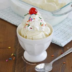 homemade vanilla ice cream topped with whipped cream, sprinkles and cherry in a white sundae bowl