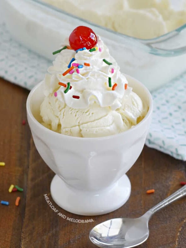 homemade vanilla ice cream topped with whipped cream, sprinkles and cherry in a white sundae bowl