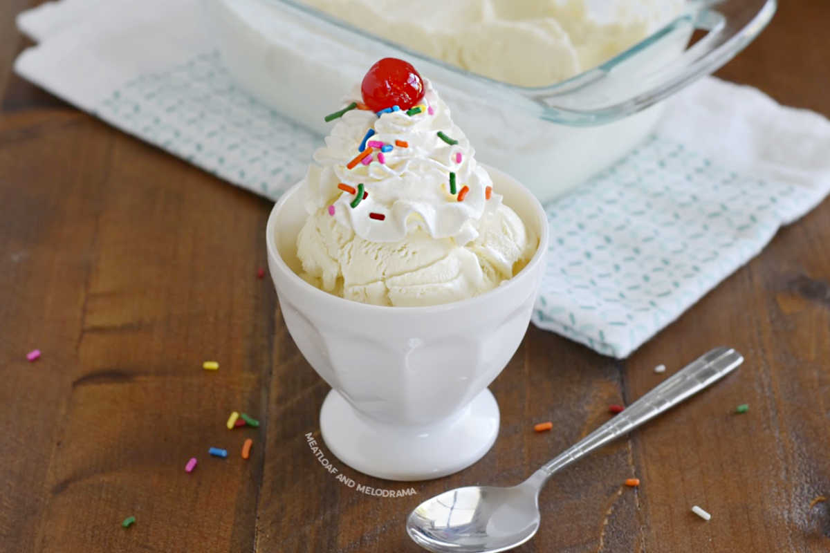 homemade vanilla ice cream topped with whipped cream, sprinkles and cherry in a white sundae bowl