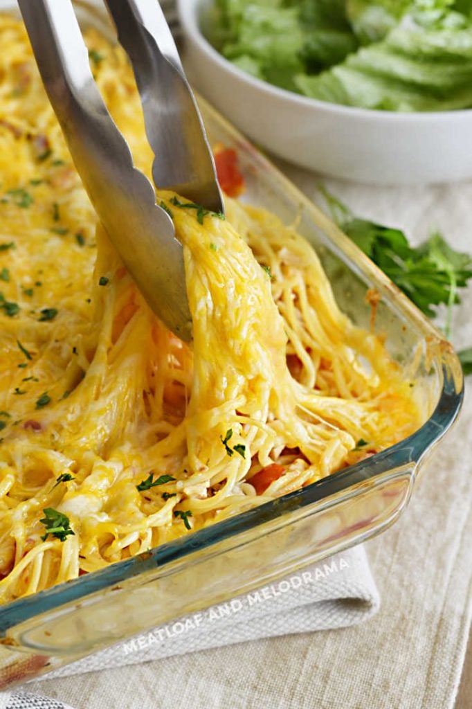 tongs holding up cheesy chicken spaghetti in baking dish