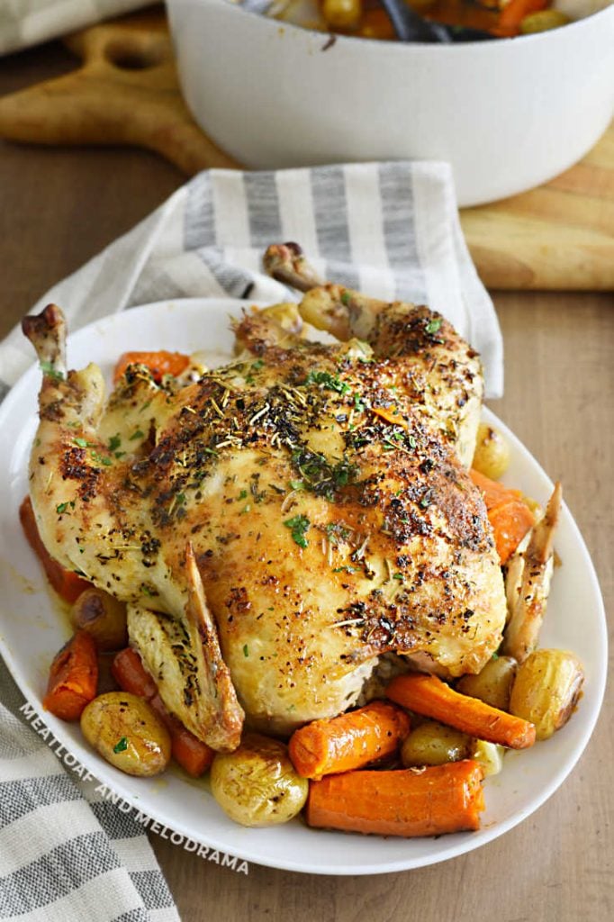 roast chicken over carrots and potatoes on a white platter