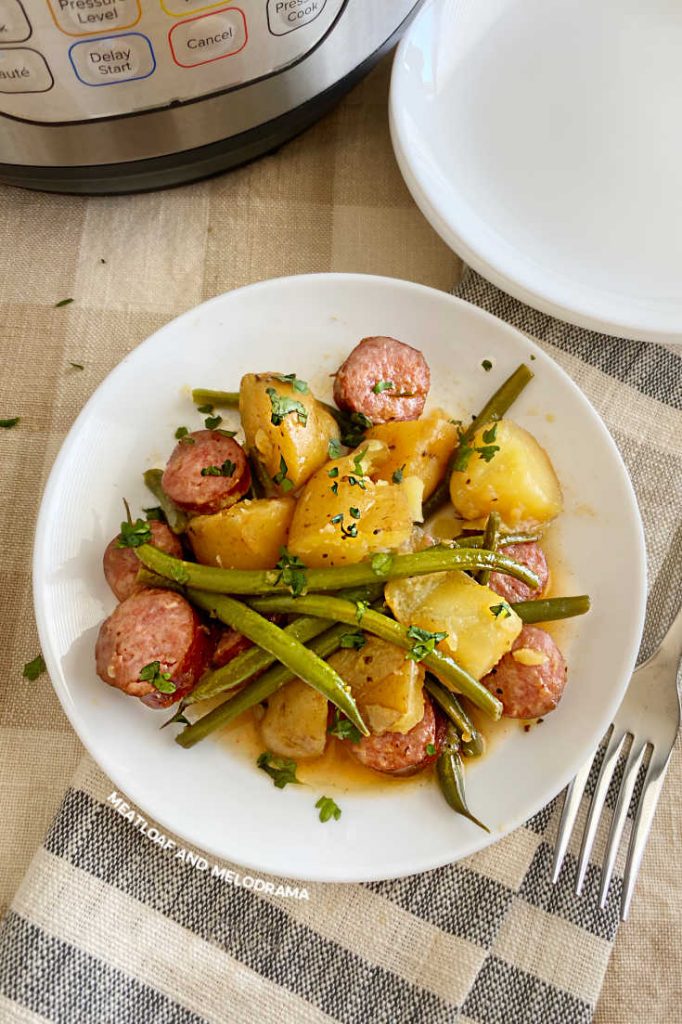 sliced potatoes with kielbasa and green beans on a white plate by an instant pot