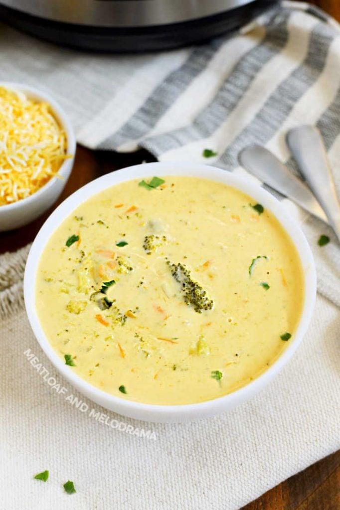 broccoli cheddar cheese soup in a white bowl with shredded cheese on the side