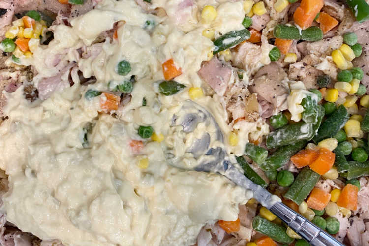 chicken mixed with cream of celery soup and mixed vegetables in a baking dish