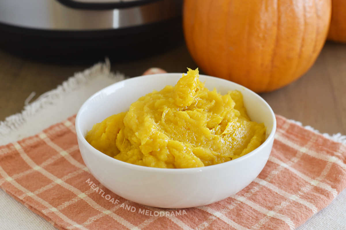 bowl of cooked pumpkin puree with instant pot pressure cooker and whole sugar pumpkin in background