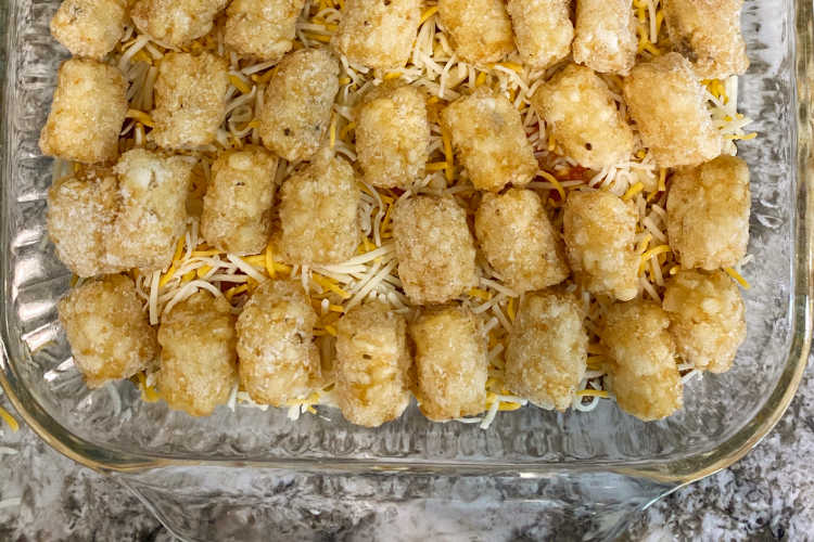 tater tots over mexican blend shredded cheese in a baking dish