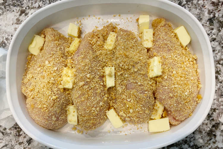 breaded chicken breasts in casserole dish with butter on top