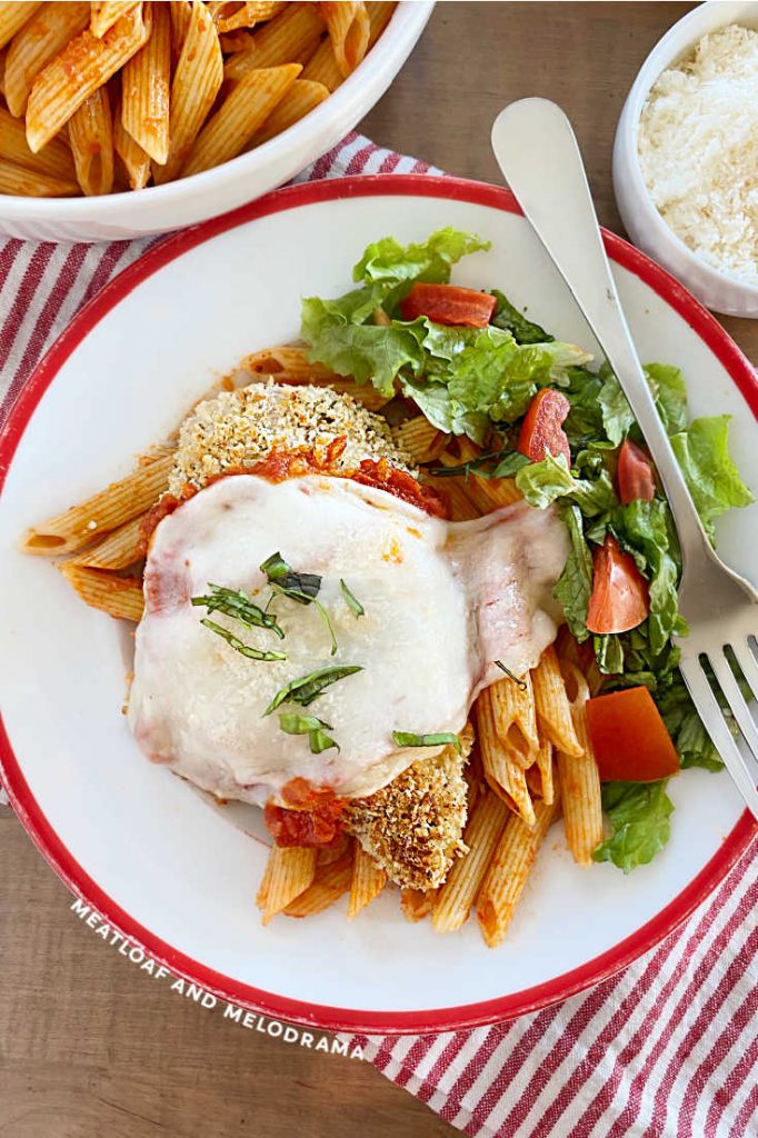 panko coated chicken breast with marinara and melted cheese on a plate with penne pasta and salad