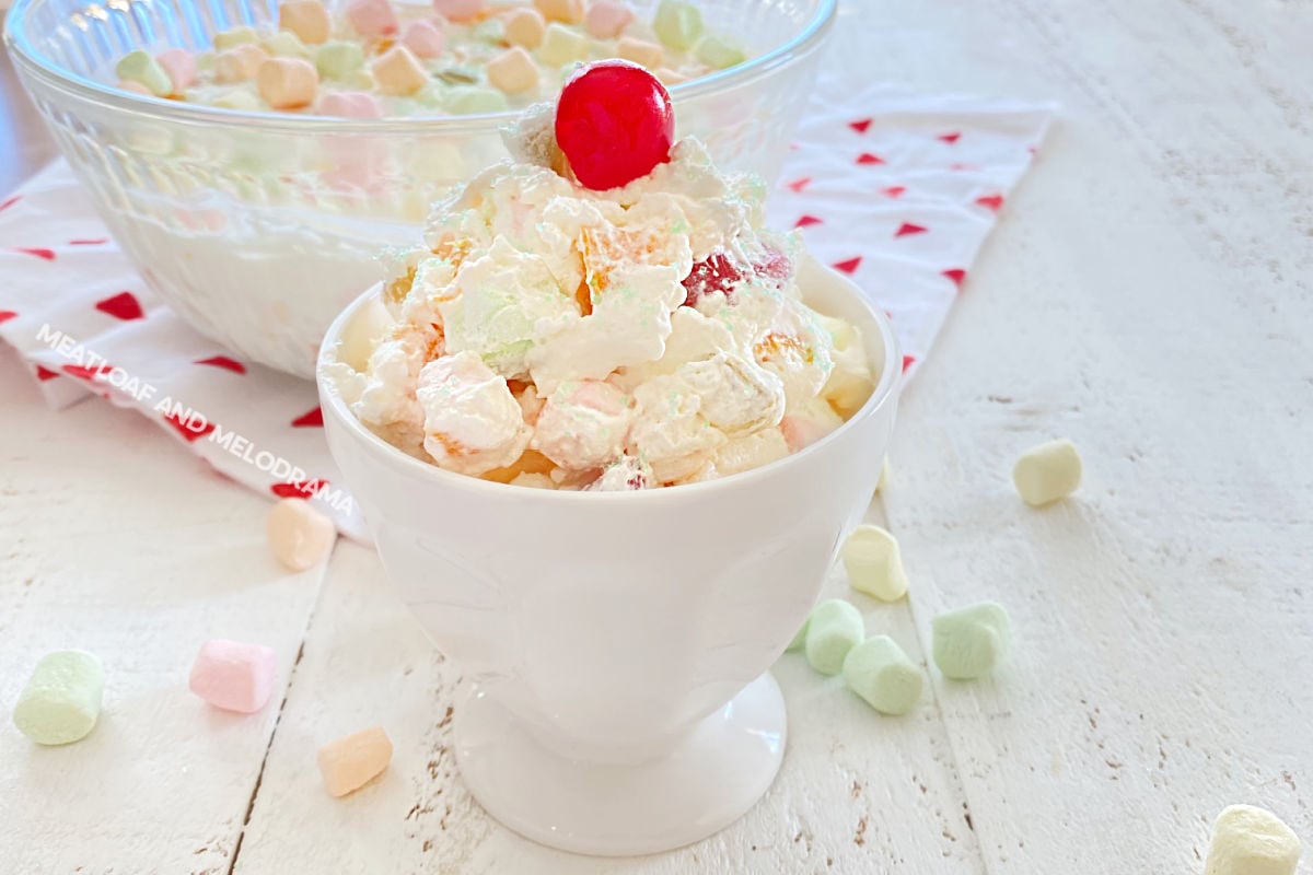 marshmallow fruit salad with cool whip and maraschino cherry on top in sundae dish