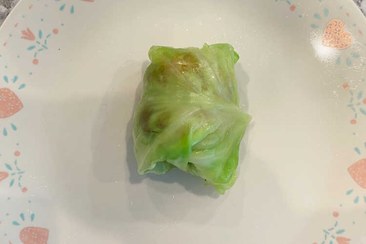 meat rolled up in uncooked cabbage roll on a plate