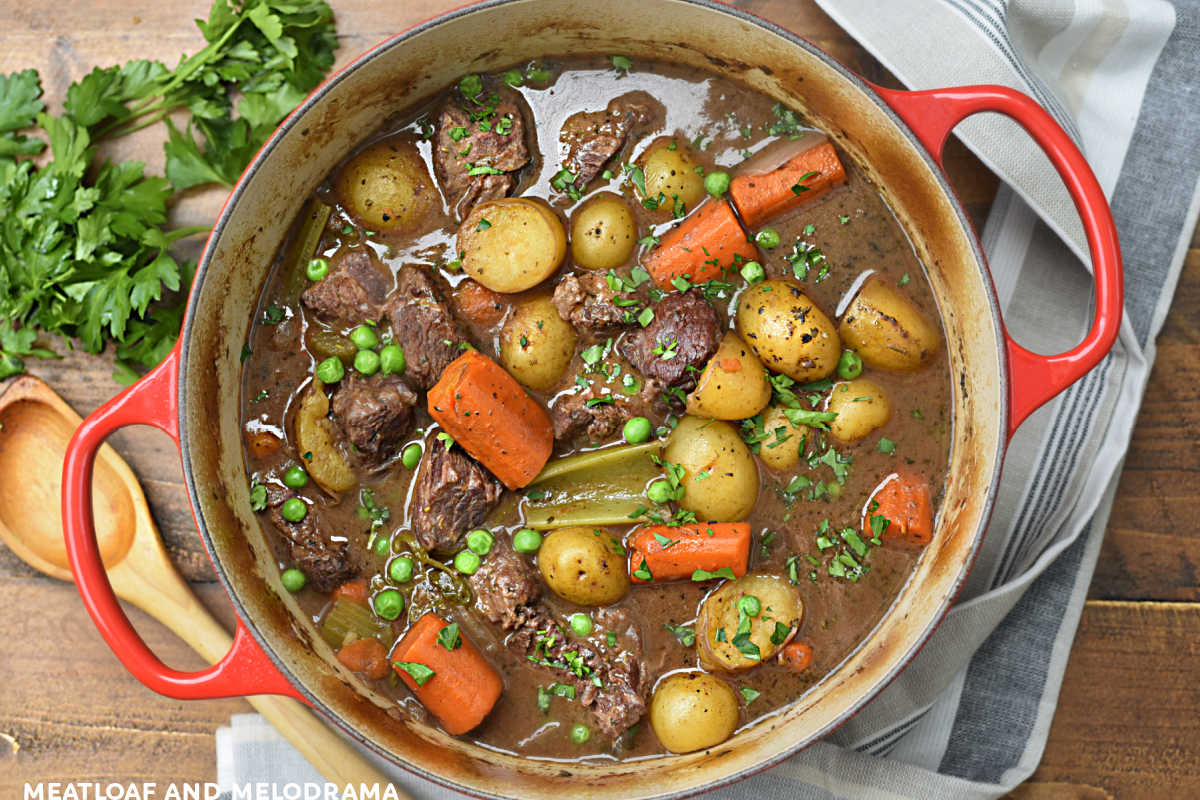 beef stew with carrots, potatoes. peas and celery in a red dutch oven
