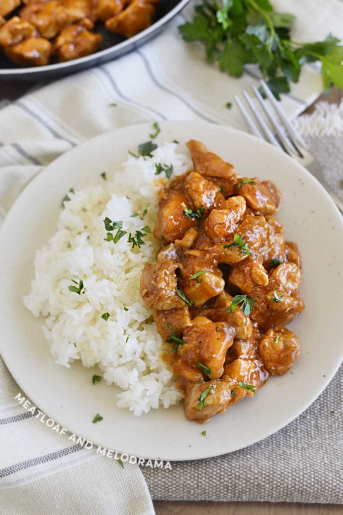 bourbon chicken over jasmine rice on a white plate with parsley