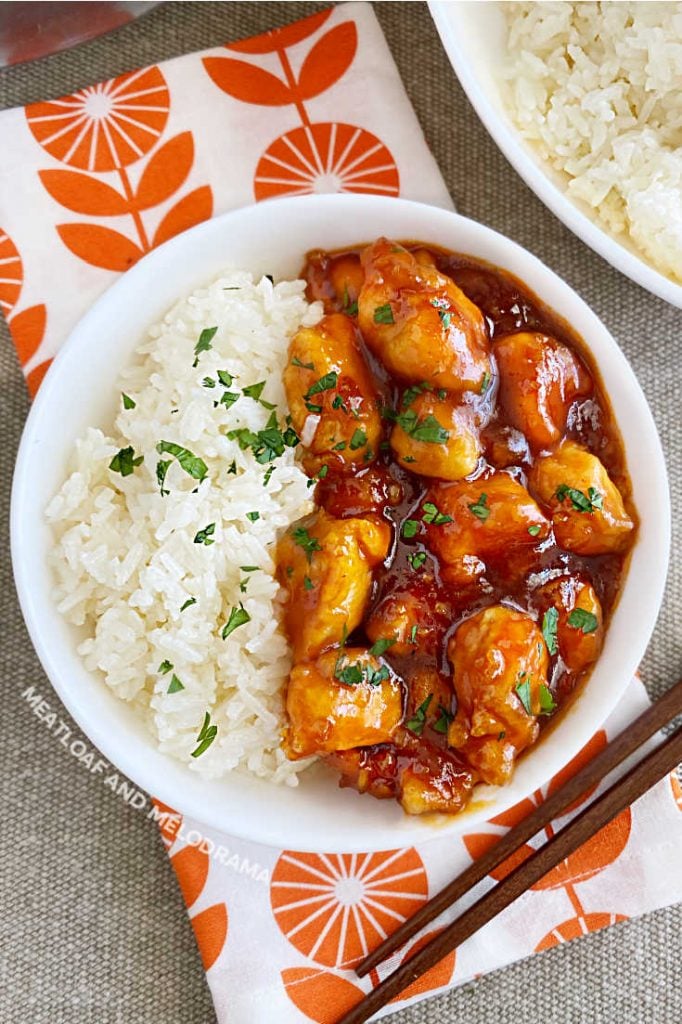 bowl of orange chicken pieces and rice on the table