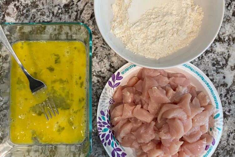 beaten eggs, cubed chicken breasts and flour on the counter