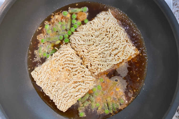 instant ramen noodles and frozen vegetables in broth in skillet